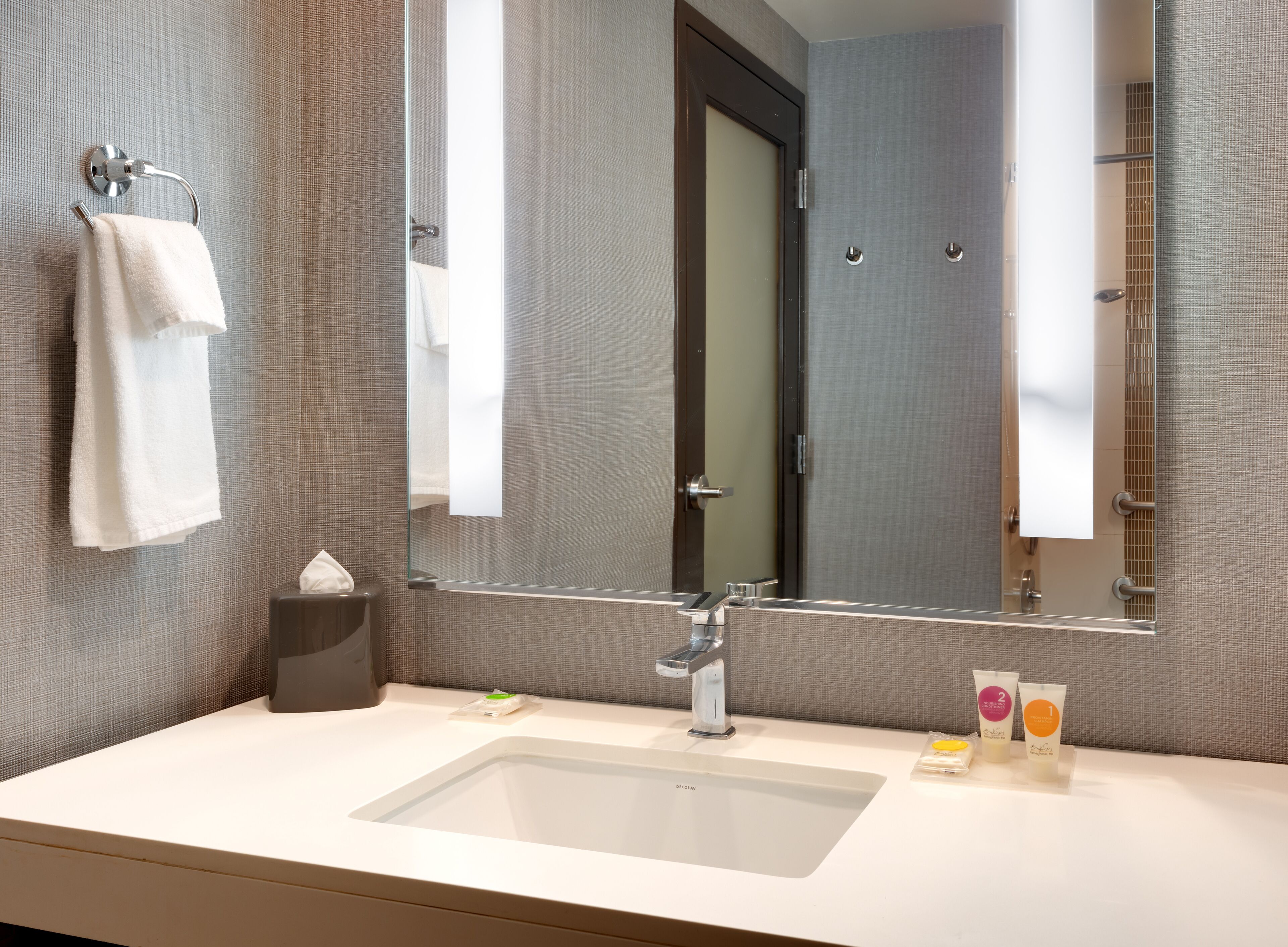 A modern bathroom with a large mirror, a sink, and toiletries.