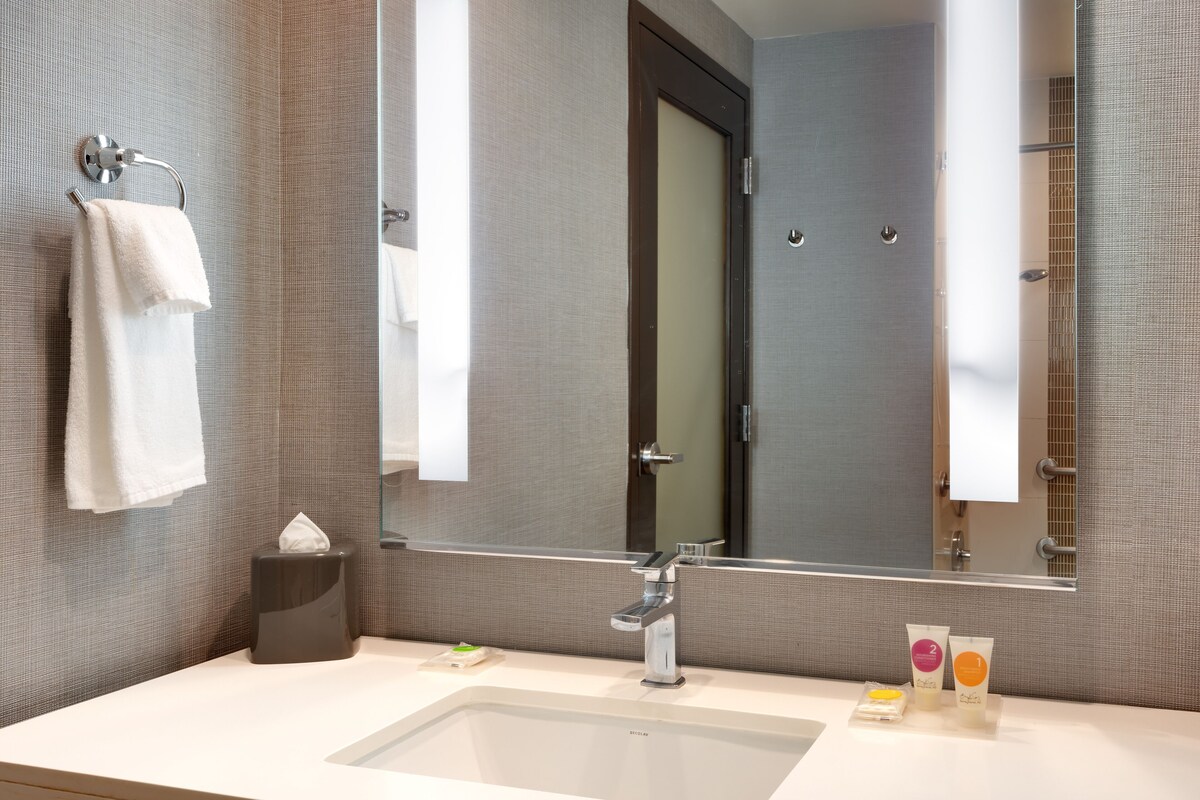 A modern bathroom with a large mirror, a sink, and toiletries.