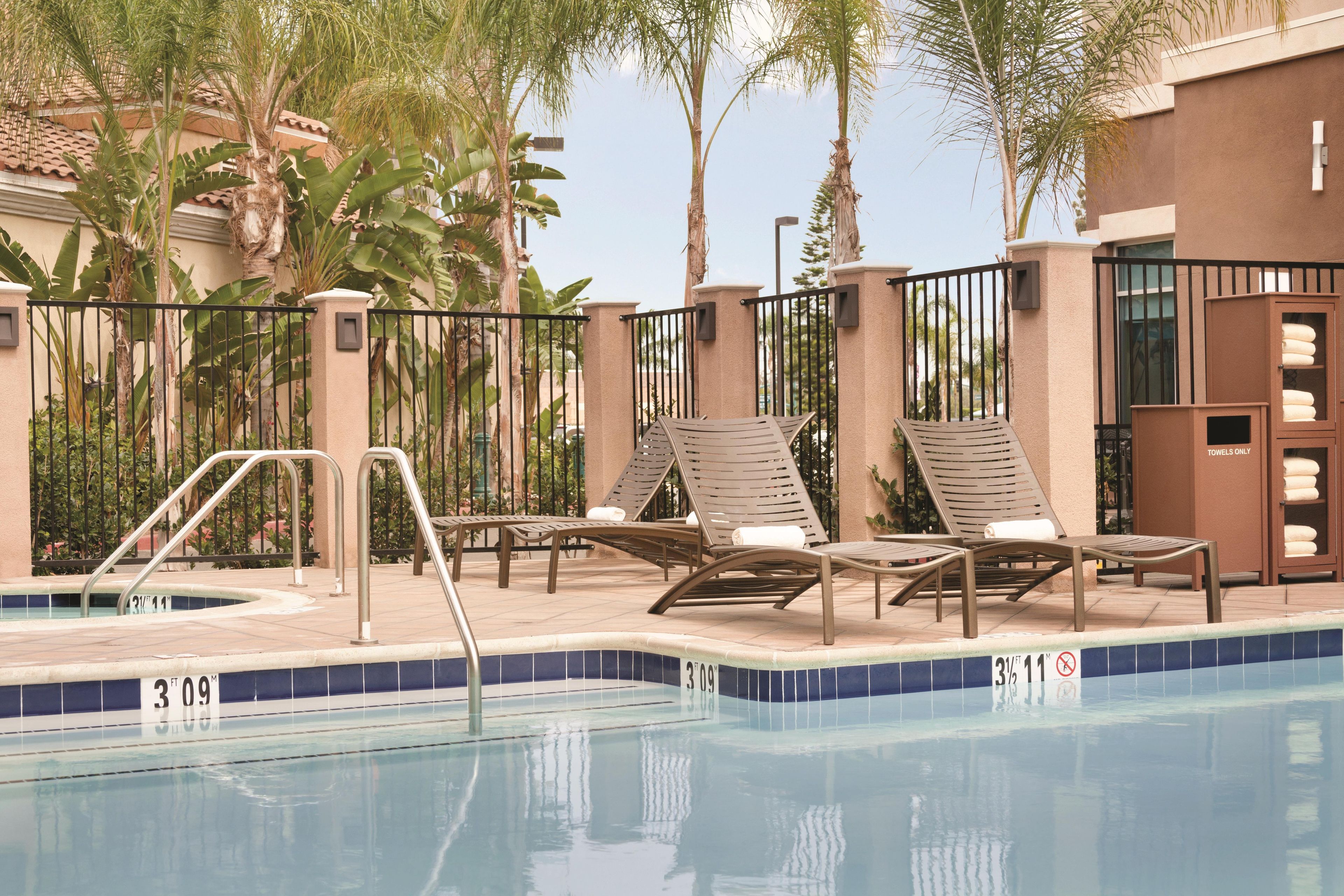 Zona de piscina con sillones de descanso y un perchero para toallas.