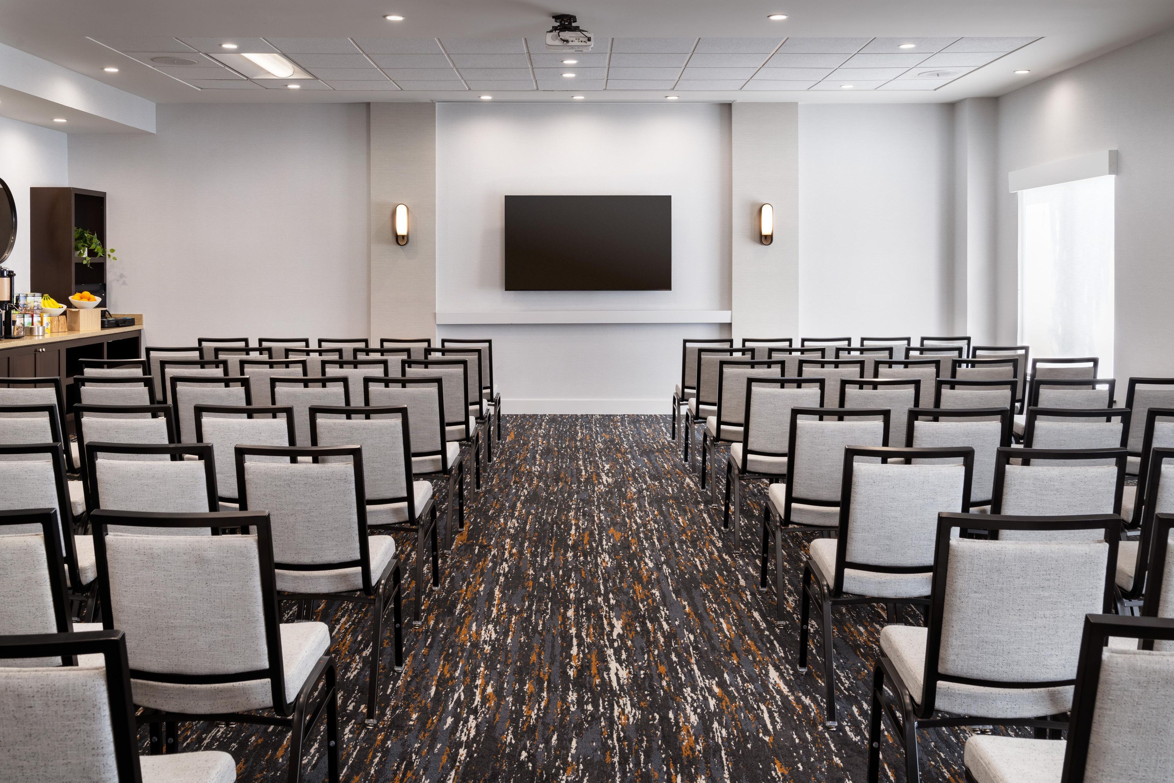 A conference room with rows of chairs, a large screen, and a projector.
