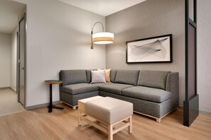 Una sala moderna con un sofá seccional gris, una mesita redonda, un banco, una lámpara de pie y una obra de arte abstracta enmarcada en la pared.