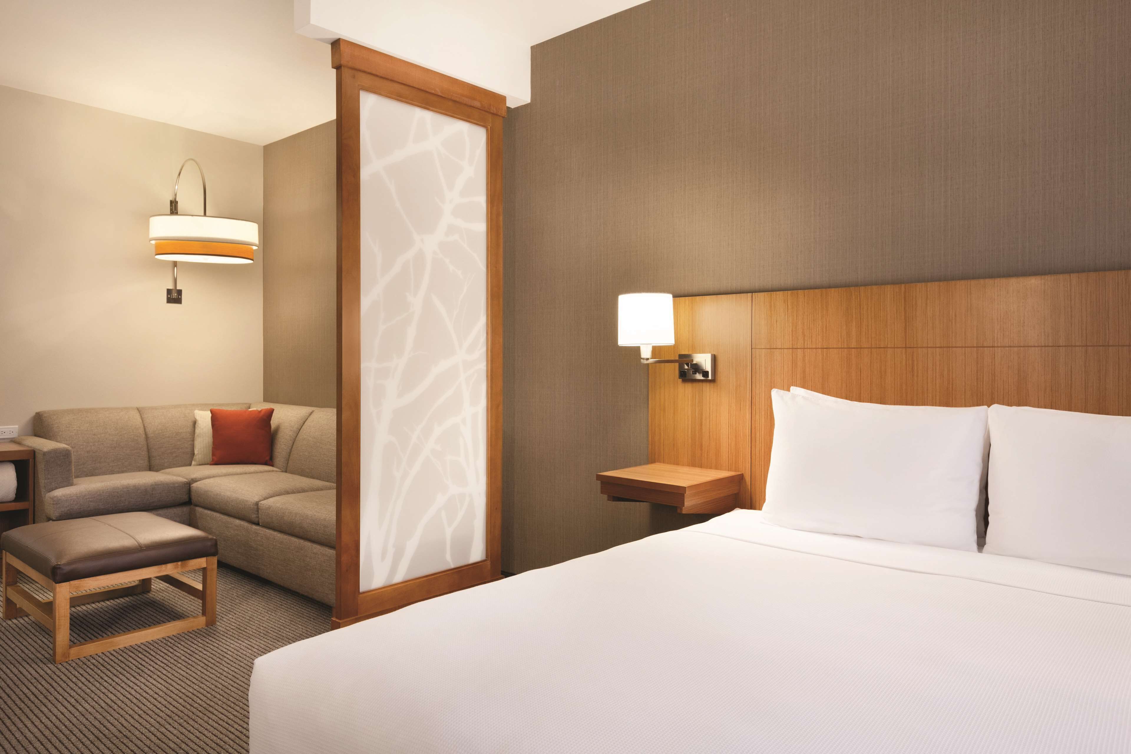 Une chambre d’hôtel avec un lit, un canapé, une table de chevet et une lampe fixée au mur.