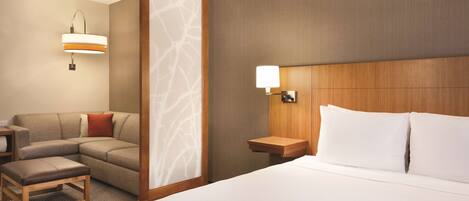 Une chambre d’hôtel avec un lit, un canapé, une table de chevet et une lampe fixée au mur.