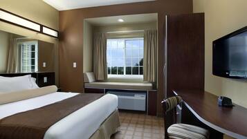 A hotel room with a bed, a desk, a chair, a television, and a window with curtains.