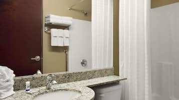 A bathroom with a granite countertop sink, a mirror, a towel rack with folded towels, a shower curtain, and a toilet.