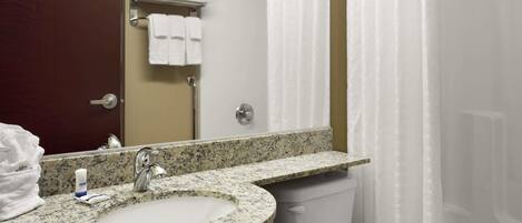 Un baño con lavamanos de encimera de granito, un espejo, toalleros con toallas dobladas, cortina de ducha y un inodoro.