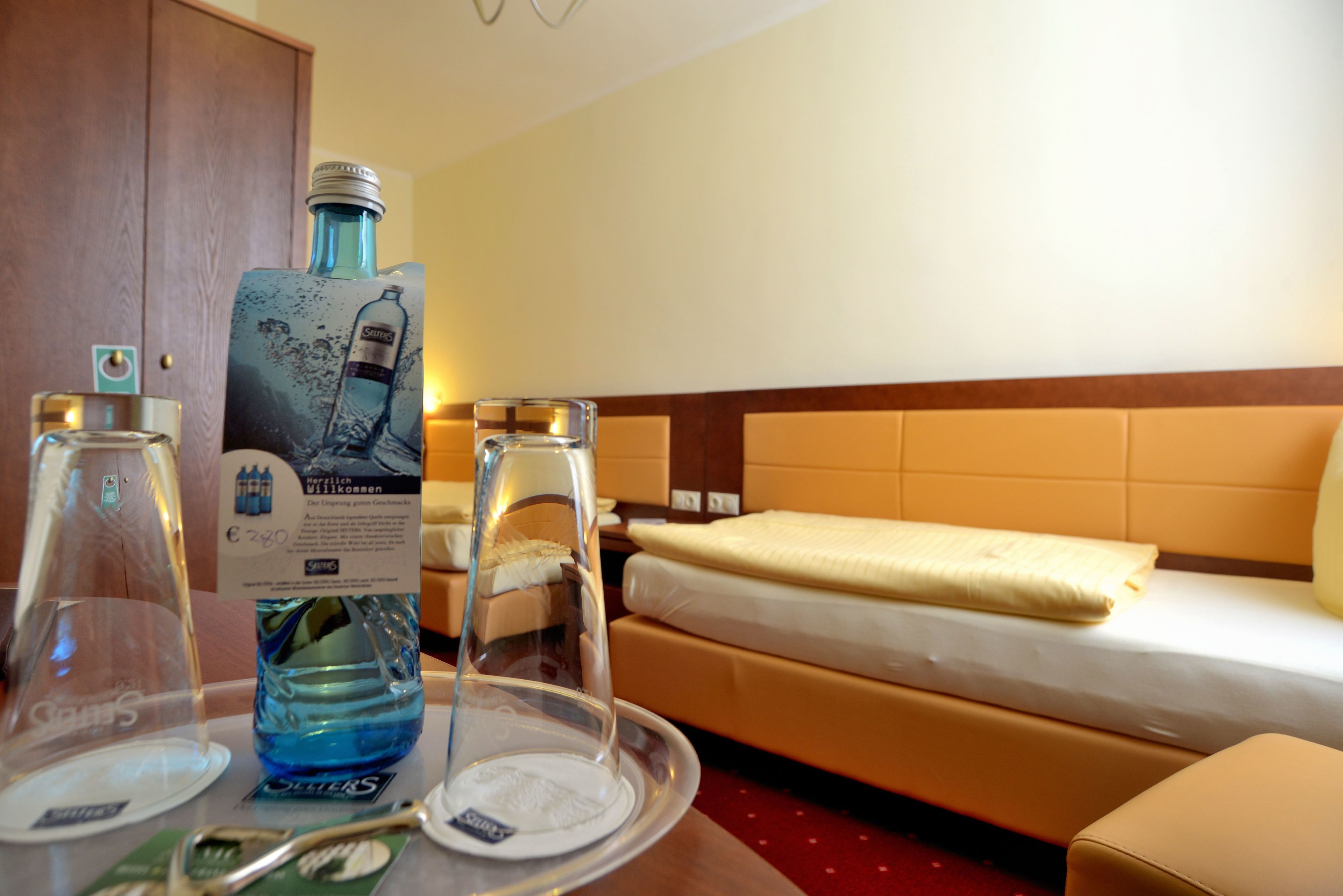 Habitación de hotel con una cama, una mesita de noche con un vaso de agua, una botella de agua y una bandeja con un vaso y una cuchara.