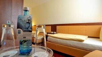 Habitación de hotel con una cama, una mesita de noche con un vaso de agua, una botella de agua y una bandeja con un vaso y una cuchara.