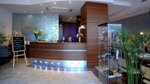 A reception area with a wooden reception desk, a stone wall with the text "ARENA CRUZ," and a glass display case with items. - Hotel Arena City (Leipzig)