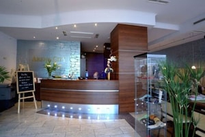 Zona de recepción con mostrador de madera, pared de piedra con el texto "ARENA CRUZ" y una vitrina con objetos.
