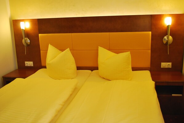 Quarto de hotel com duas camas, cada uma com cabeceira e duas luminárias de cabeceira.
