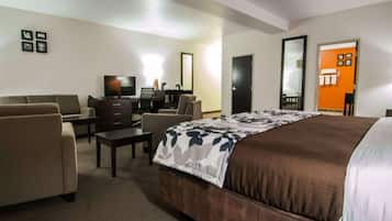 A hotel room with a bed, two armchairs, a desk, a television, and a bathroom visible through an open door.