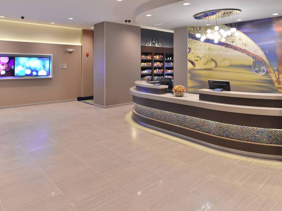 A hotel reception area with a curved reception desk, a large flat-screen TV, and a wall with a decorative image.