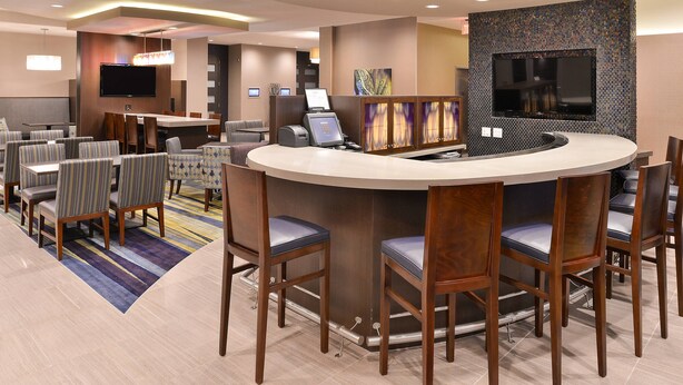 A hotel lobby with a reception desk, seating area, and a large flat-screen TV mounted on the wall.