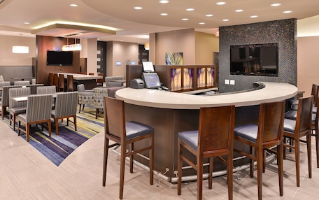 A hotel lobby with a reception desk, seating area, and a large flat-screen TV mounted on the wall.