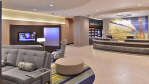 A lobby with a sofa, armchair, and ottoman, a reception desk, a television screen, and a large wall mural.