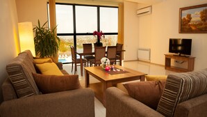 A living room with a sofa set, a dining table with chairs, a TV, and a large window with a view. - Panorama Resort (Yerevan)