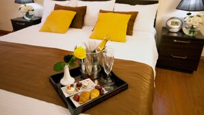 A neatly made bed with a tray of breakfast items, including croissants, fruit, and a bottle of champagne, in a hotel room. - Panorama Resort (Yerevan)