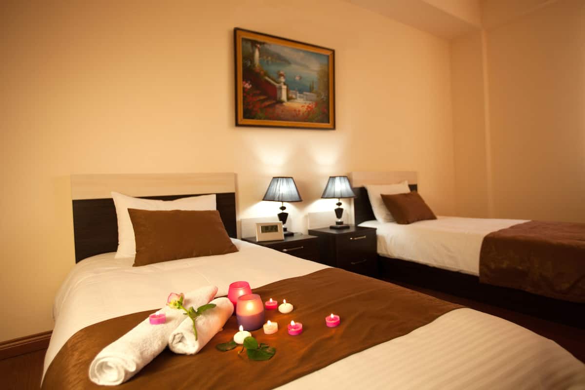 Ein Hotelzimmer mit zwei Betten, einem Bild an der Wand und einer dekorativen Anordnung aus Kerzen und Blumen auf den Betten.