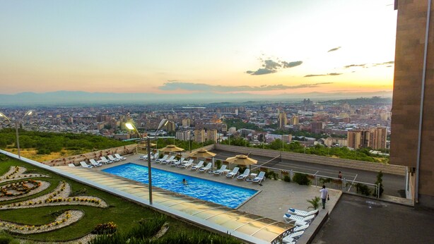 A rooftop pool with lounge chairs and a view of a cityscape at sunset. - Panorama Resort (Yerevan)