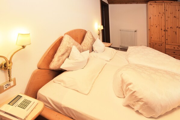 A hotel room with a wooden headboard, a bedside lamp, a telephone, and a radiator.