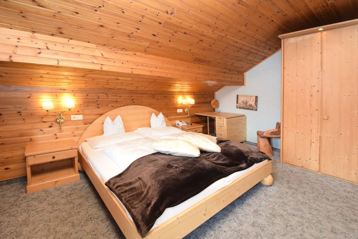 A wooden-paneled bedroom with a bed, bedside lamps, and a wardrobe.