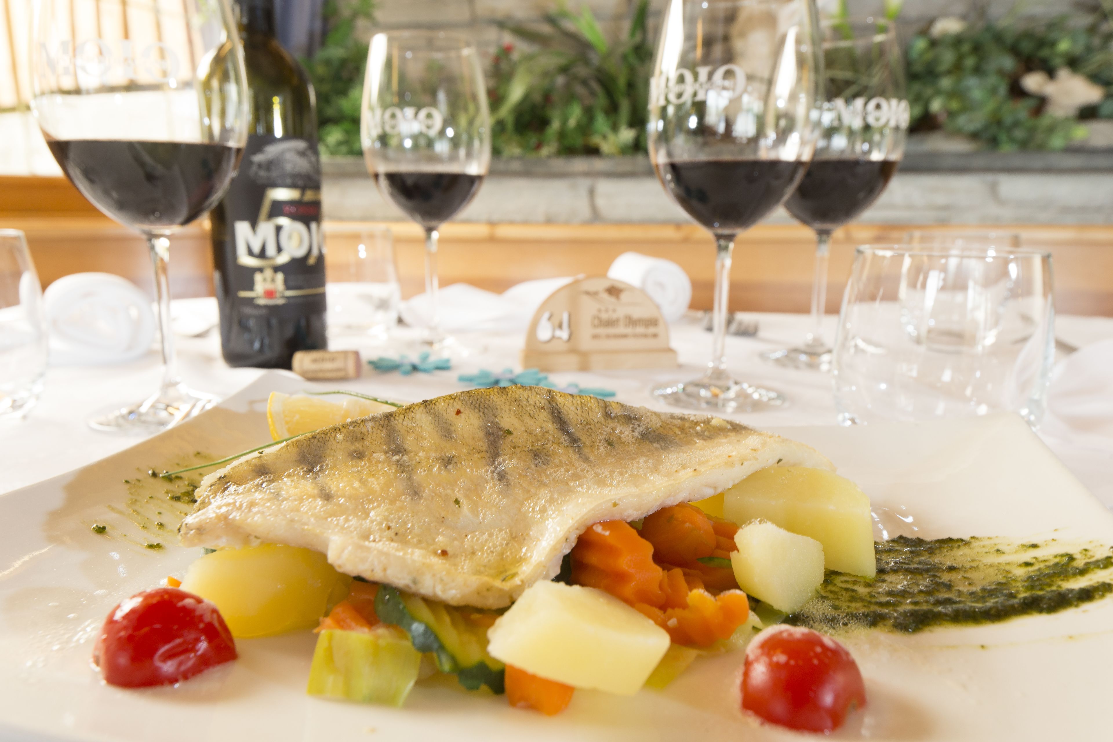 Un plato de pescado con verduras y una botella de vino sobre una mesa.