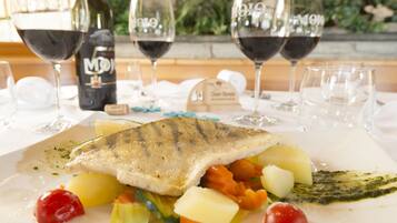 Un plato de pescado con verduras y una botella de vino sobre una mesa.
