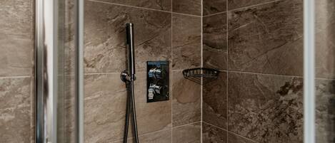A shower area with a glass door, a handheld showerhead, and a control panel.