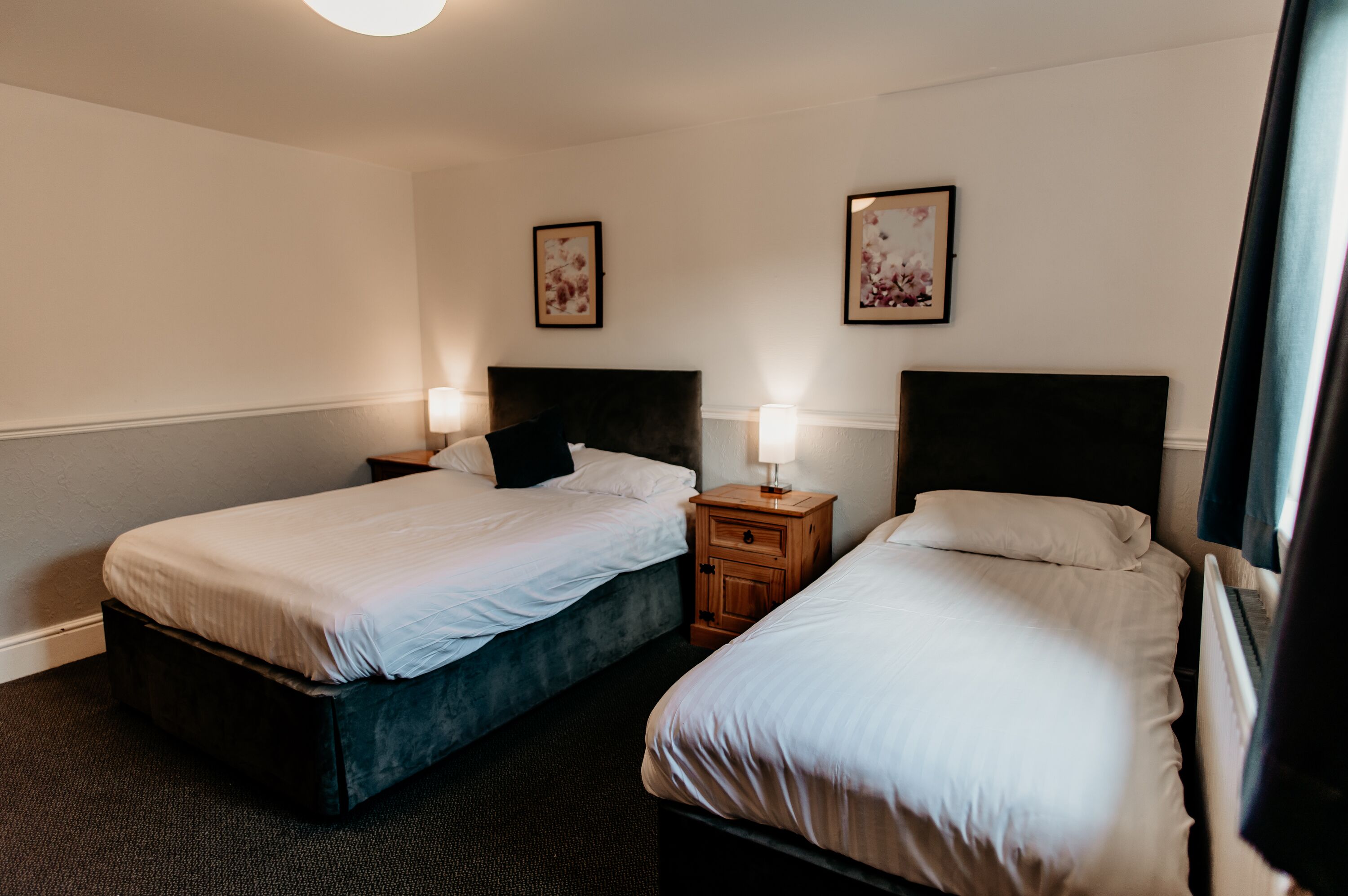A hotel room with two beds, a nightstand with a lamp, and framed artwork on the wall.