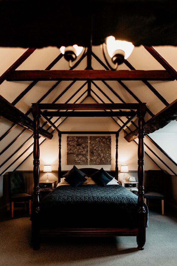 A bedroom with a four-poster bed, two bedside lamps, a nightstand, and a painting on the wall.