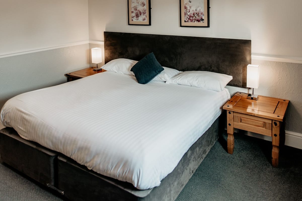 A neatly made bed with a dark headboard, two bedside tables with lamps, and two framed artworks on the wall.