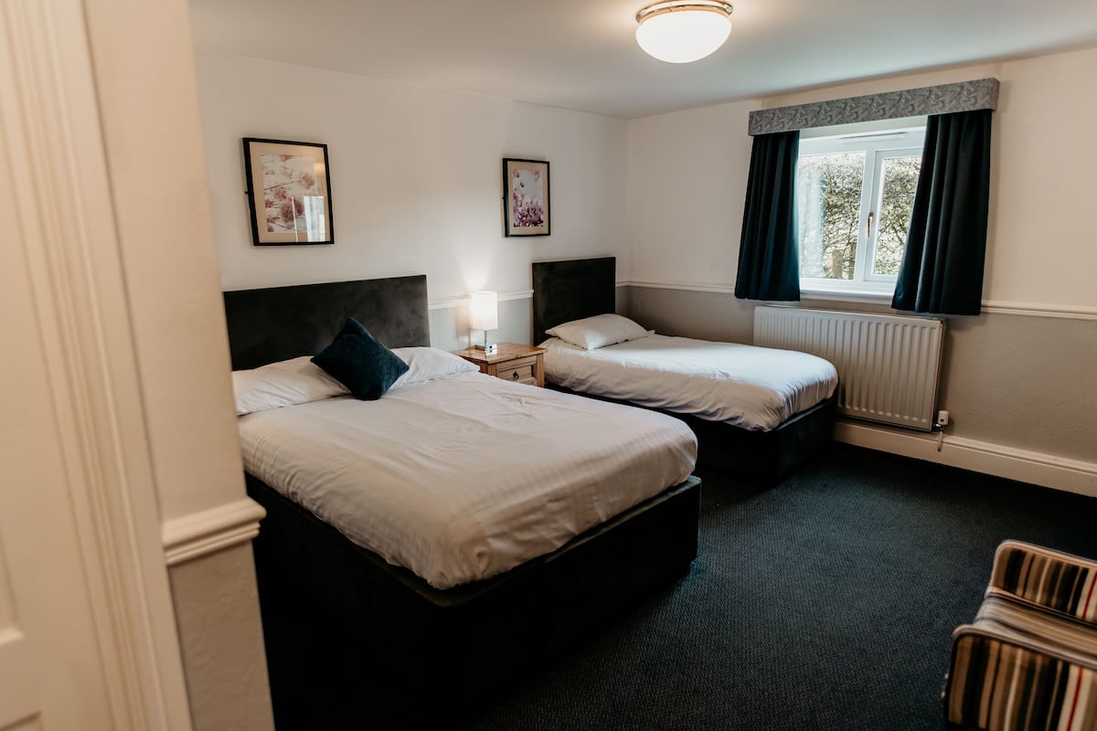 A hotel room with two beds, a window with curtains, a radiator, and artwork on the walls.