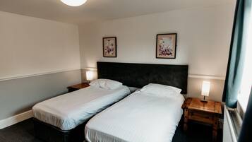 A hotel room with two single beds, a dark headboard, bedside lamps, and framed floral artwork on the wall.