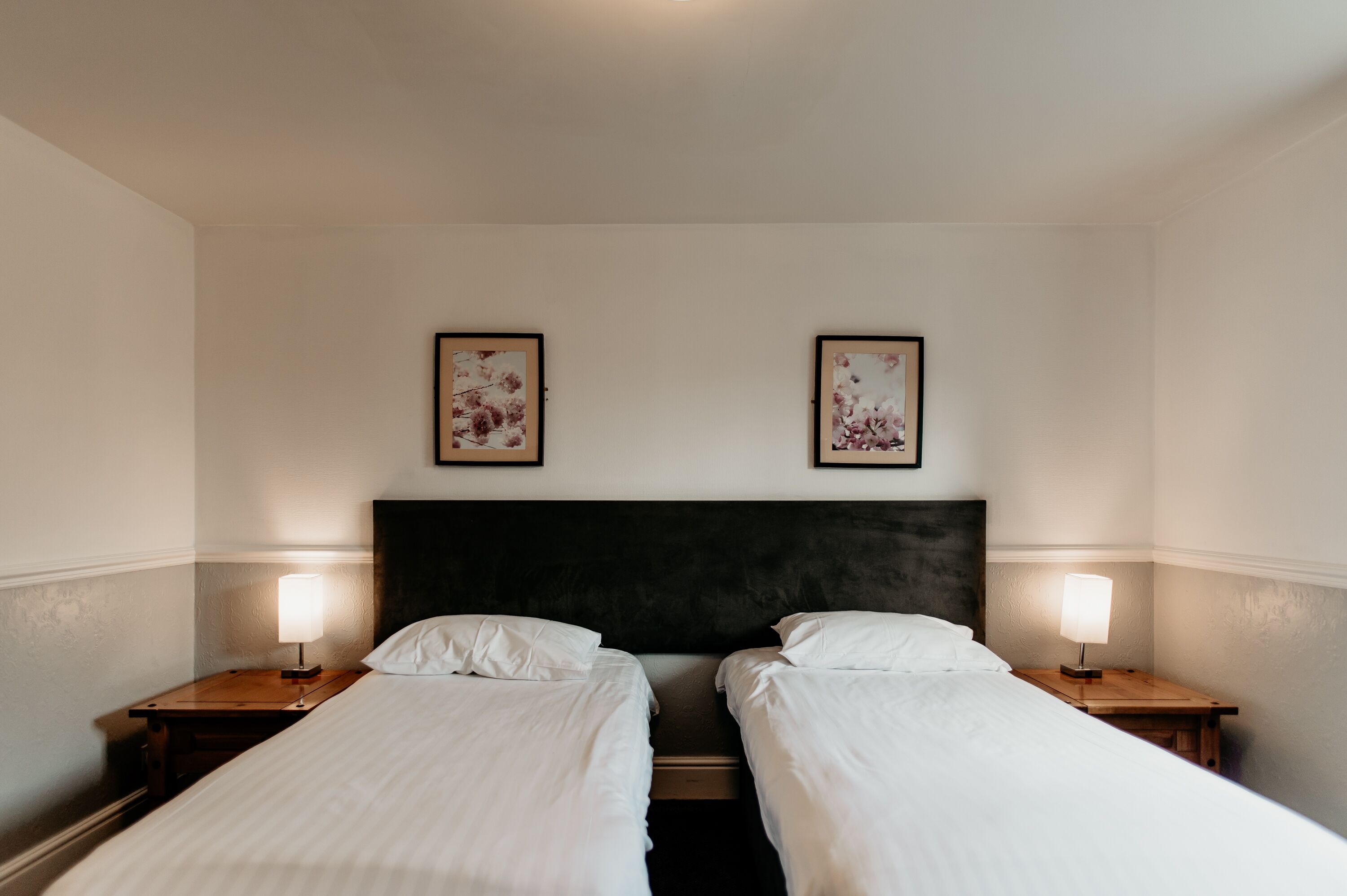 A hotel room with two single beds, a dark headboard, and two bedside lamps.