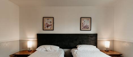 Een hotelkamer met twee eenpersoonsbedden, een donker hoofdbord en twee bedlampen.