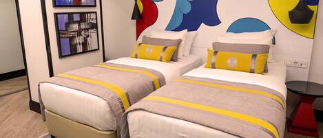 A hotel room with two beds, each with a beige and yellow striped bedspread. There are two framed pictures on the wall, one depicting a cityscape and the other a close-up of a city street.