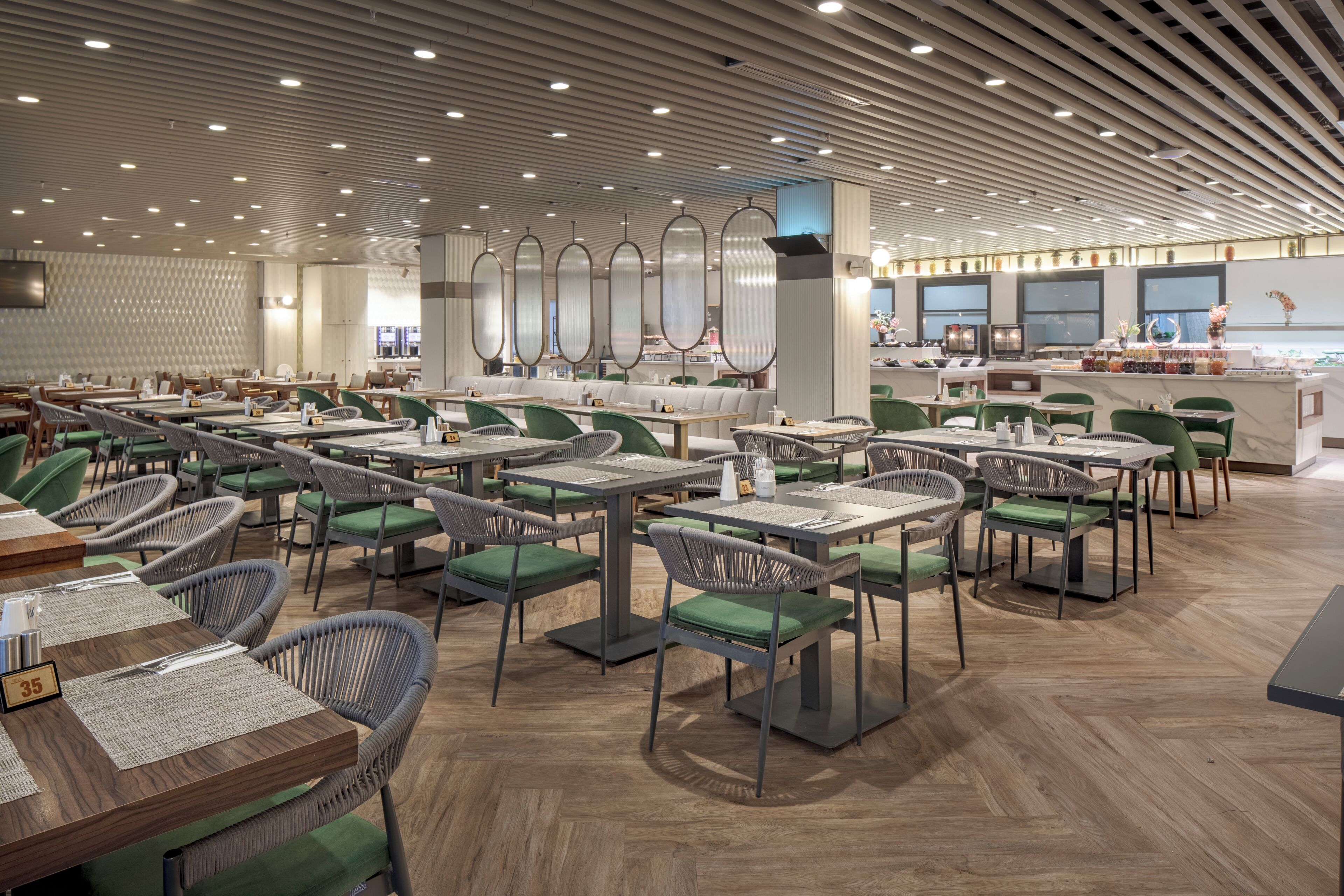 A modern restaurant with multiple dining areas, green cushioned chairs, and a central bar area.