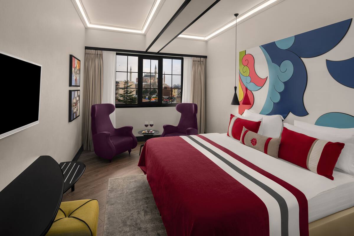 Una habitación de hotel moderna con una cama grande, televisión, escritorio y vistas a la ciudad por la ventana.