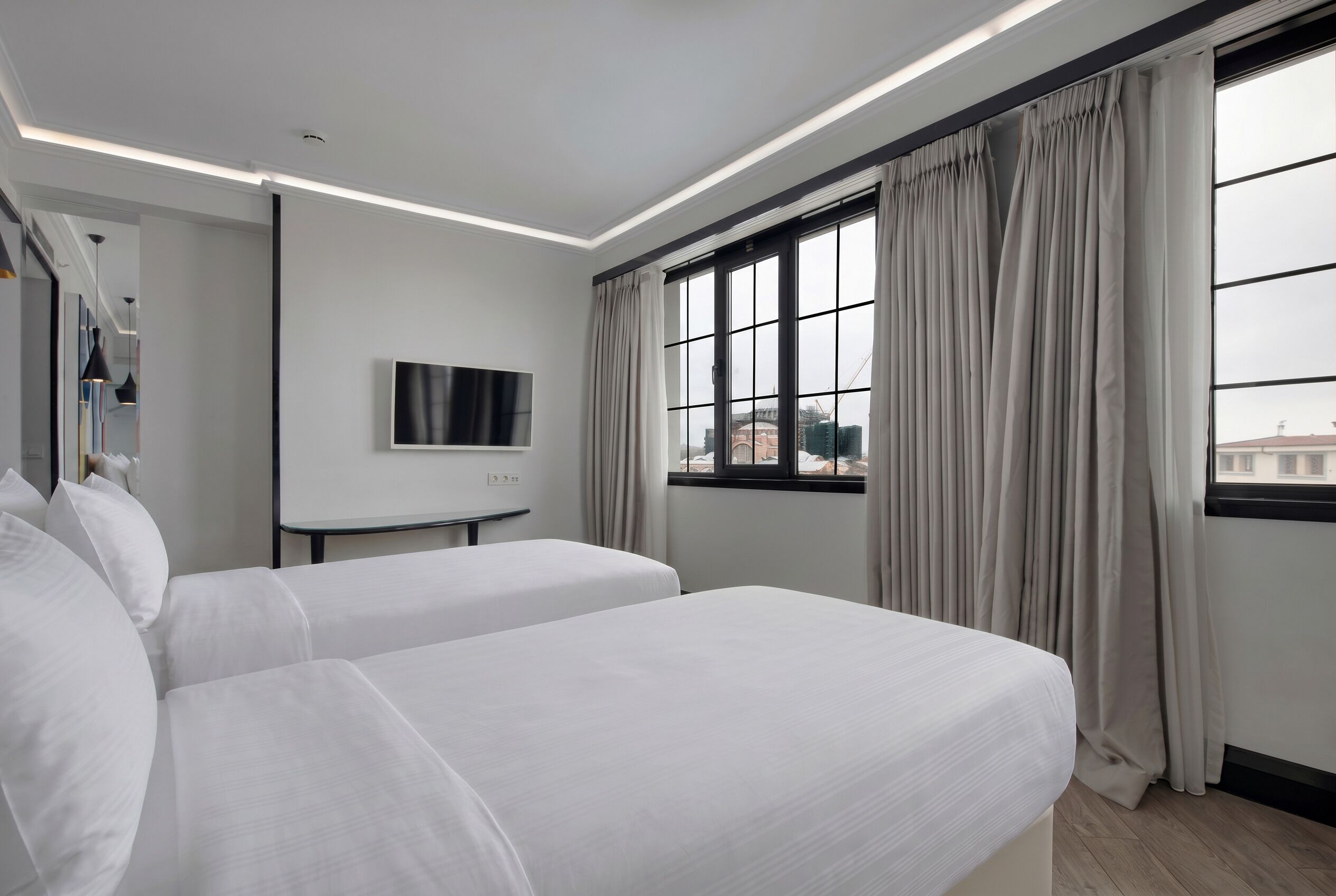 A hotel room with two beds, a TV mounted on the wall, and a window with curtains.
