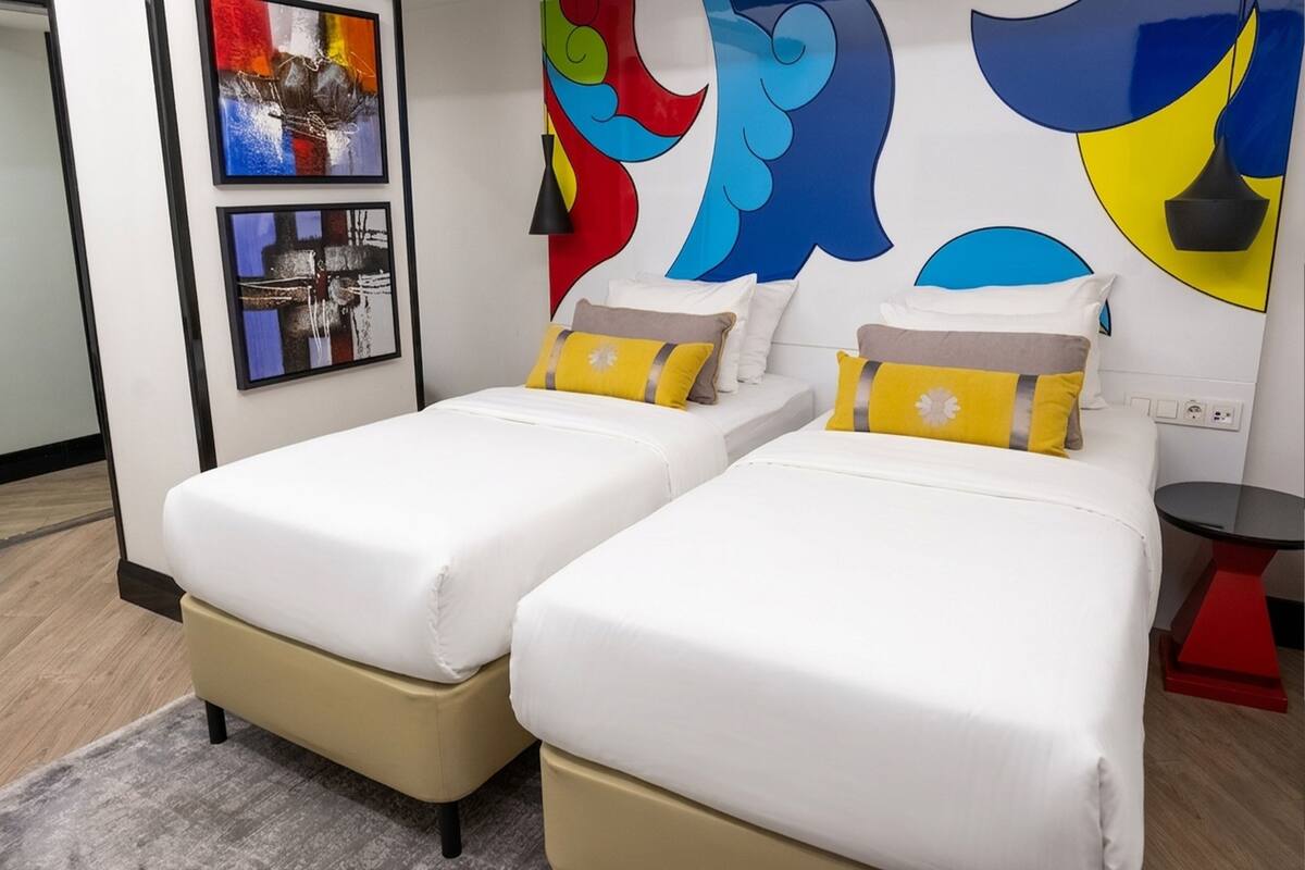 Habitación de hotel con dos camas, una mesita pequeña y un cuadro abstracto en la pared.