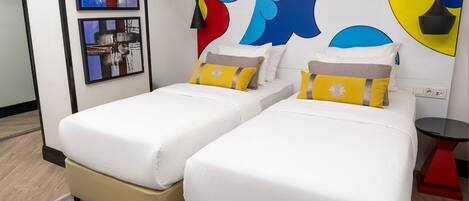 A hotel room with two beds, a small table, and abstract wall art.
