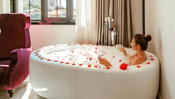 Una mujer en una bañera con pétalos de rosa y un vaso de agua.