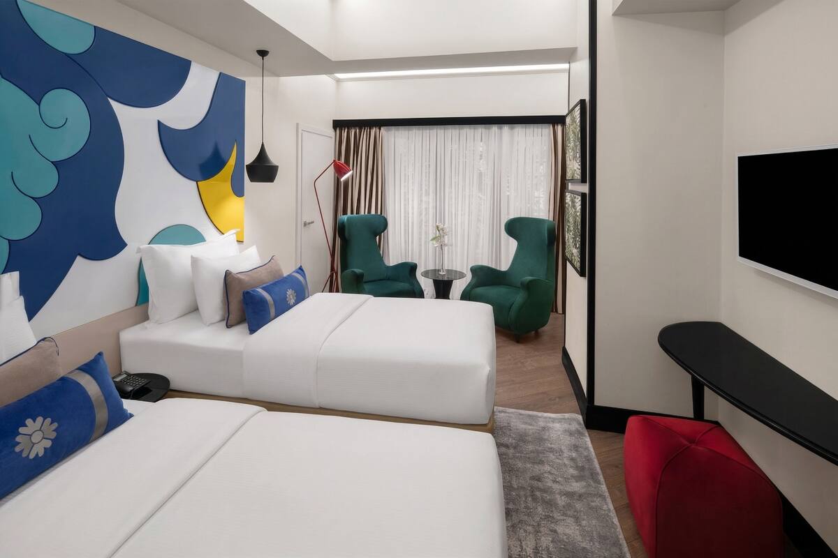 Una habitación de hotel moderna con una cama grande, dos sillones verdes, una mesita y un televisor de pantalla plana.