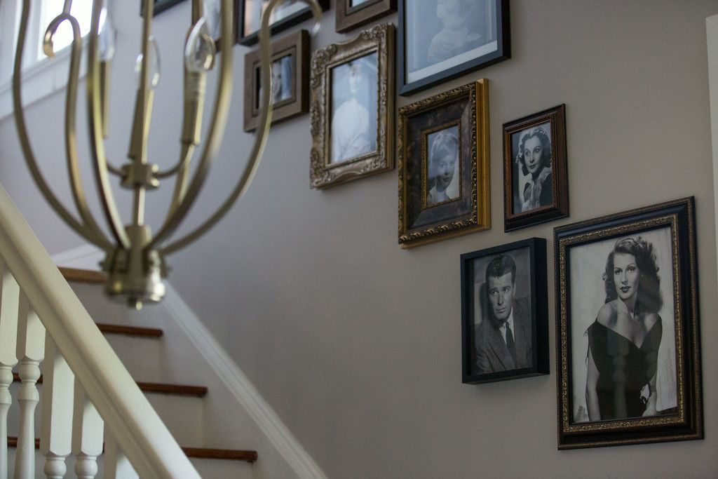 A staircase with a chandelier and framed photographs on the wall.