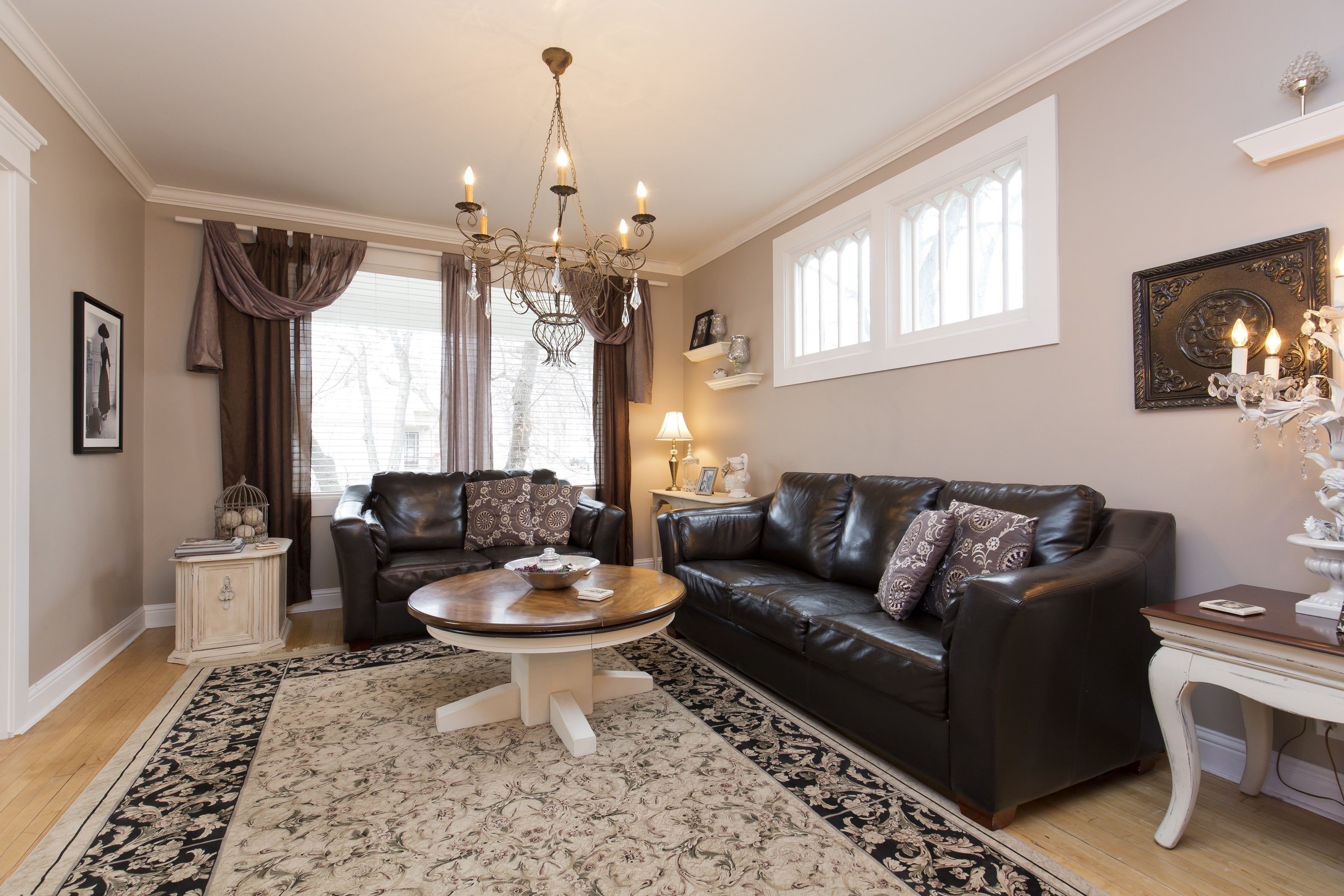 A living room with a chandelier, leather sofa, and a patterned rug.