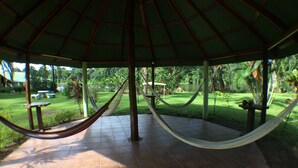 A covered outdoor area with a hammock, tiled floor, and a view of a garden and lake.