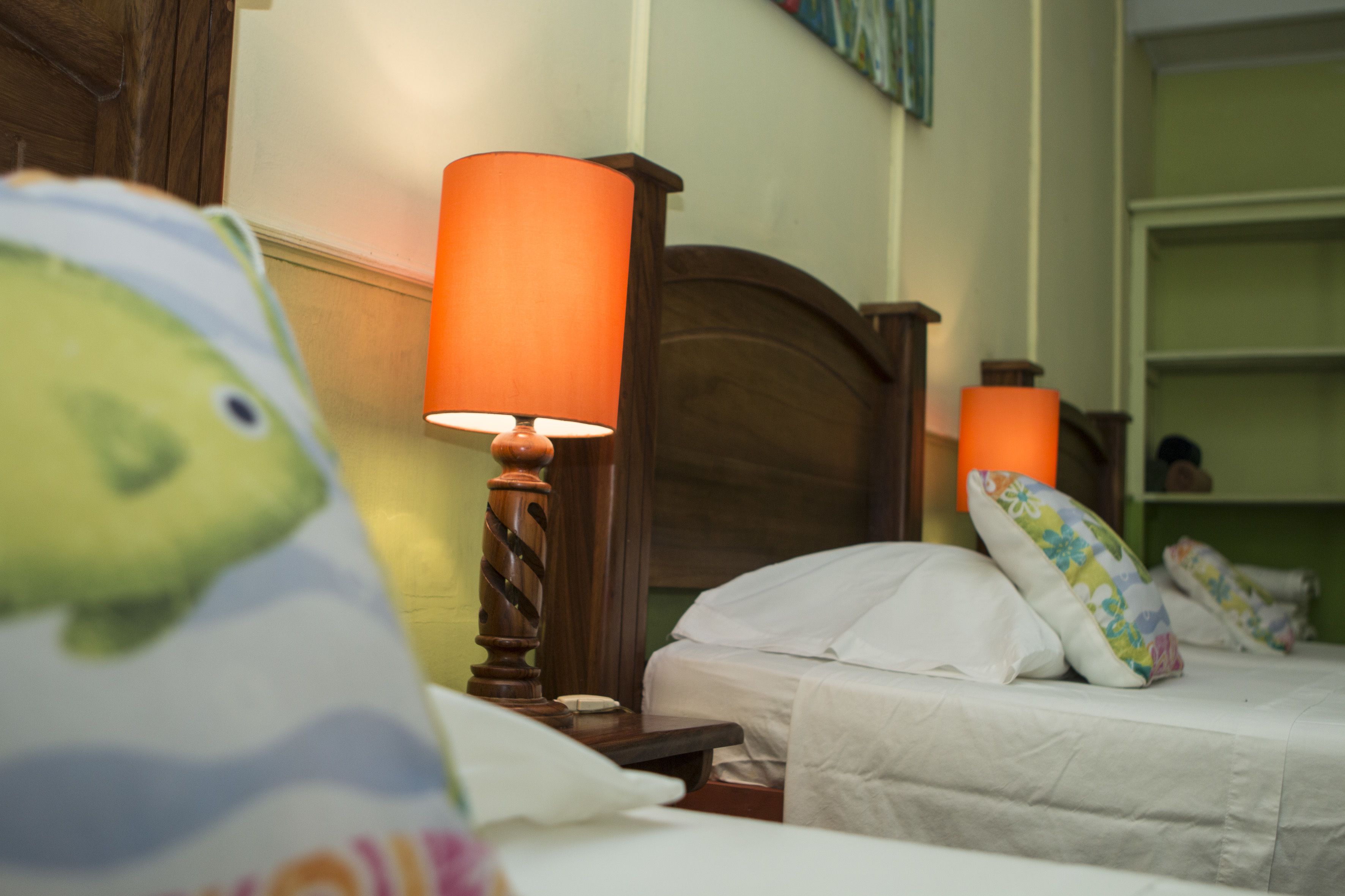 A hotel room with a wooden headboard, a bedside lamp, and a bed with white bedding and colorful pillows.