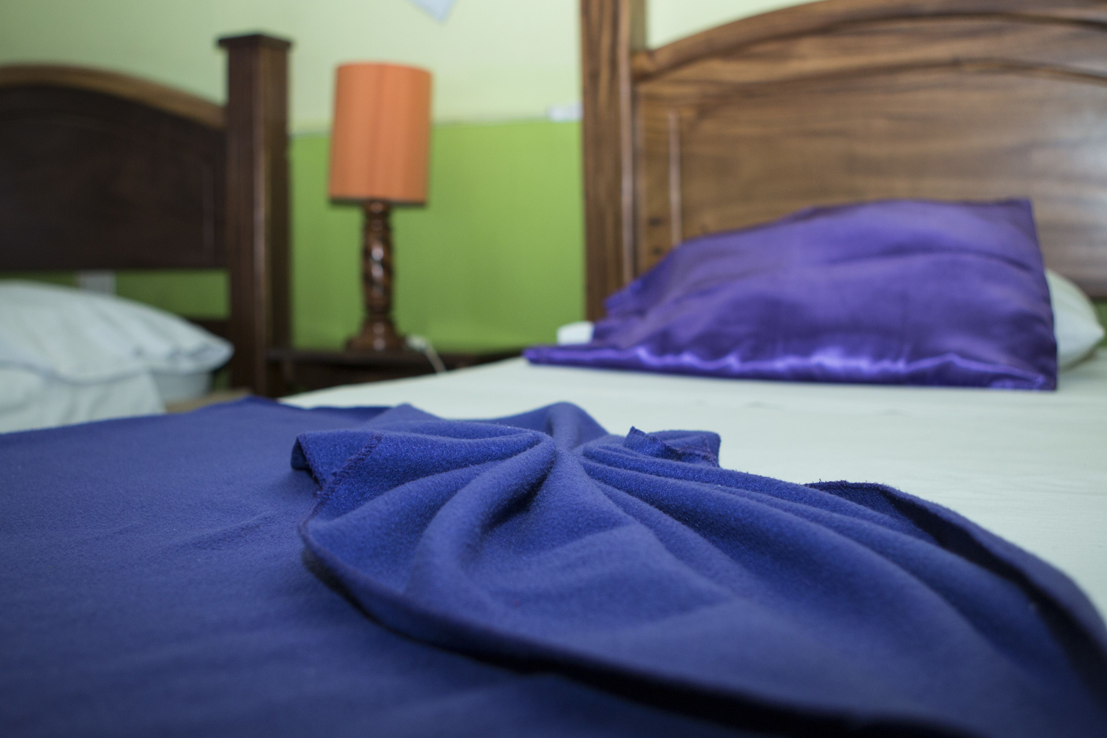 Una cama con una colcha y almohadas moradas, un cabecero de madera y una mesita de noche con una lámpara.