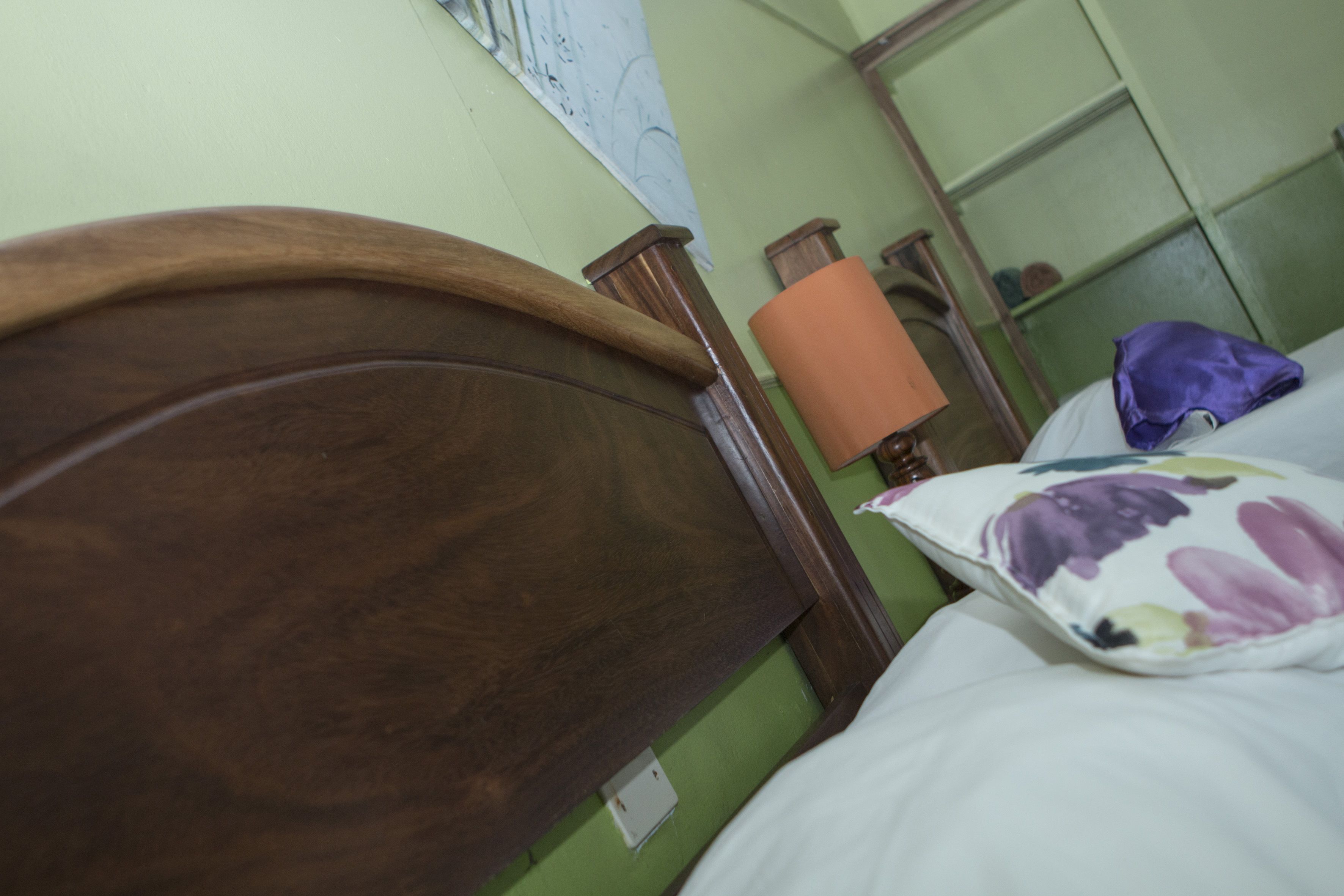 Cabecera de madera, almohada blanca con estampado floral y pared verde.